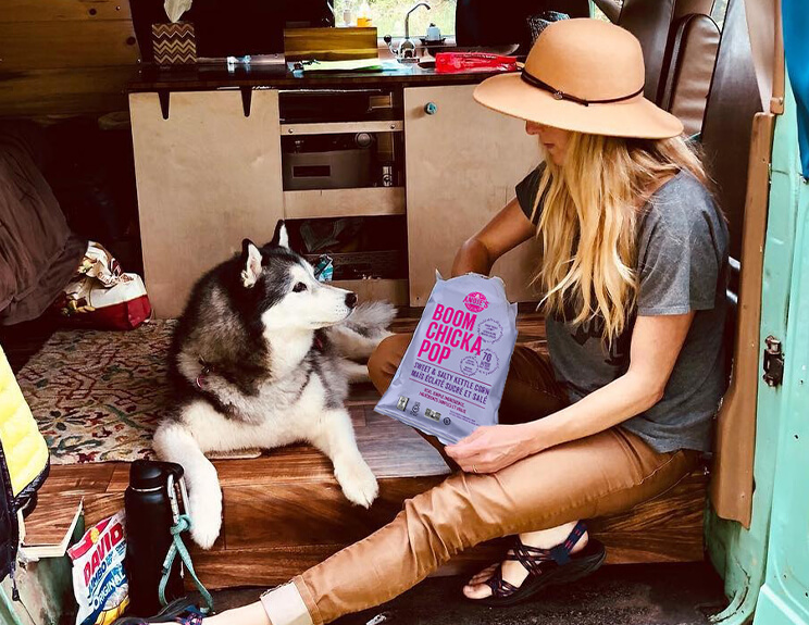 Woman eating Boom Chicka Pop beside a Husky